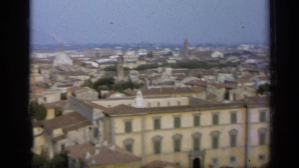 1962 8mm view over an Italian city, showing tiled roofs, pale buildings, distant domes, and dark film-frame borders.