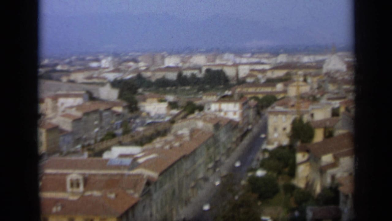 1962 Italian city panorama with a straight street, rows of tiled roofs, pale masonry buildings, and a dome in the distance.
