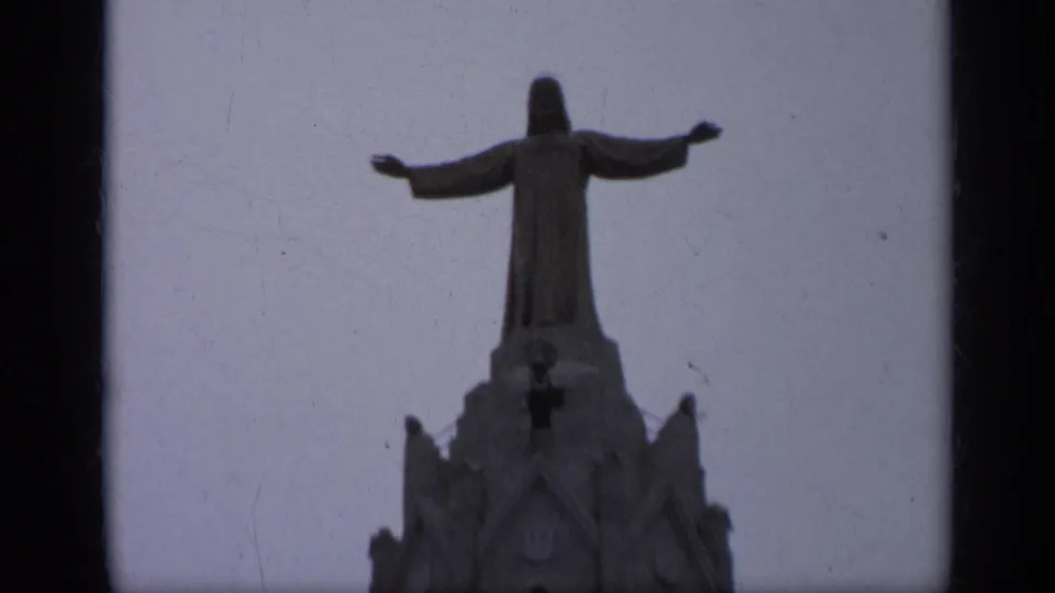 Visitor-shot 1962 Italy frame focused on the Christ statue above a Gothic-style church tower under a pale sky.