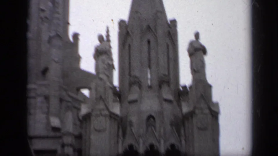 1962 Italy 8mm frame showing an ornate Gothic-style church tower with sculpted figures, crosses, and stone architectural details.
