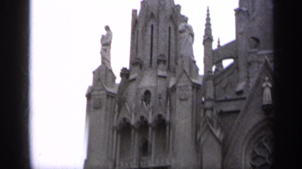 Upper stone church facade with carved figures, pointed rooflines, and dark vertical obstruction.