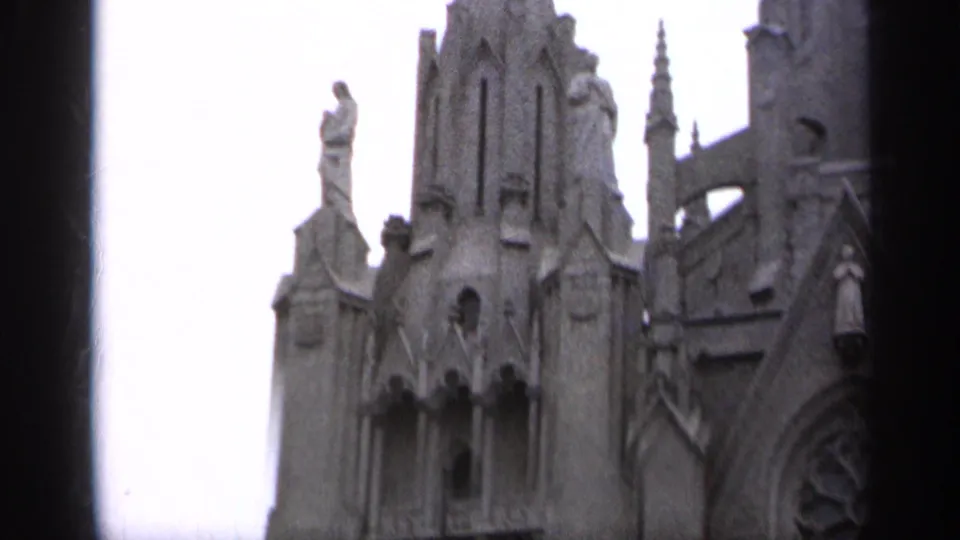 1962 Italy 8mm frame showing upper Gothic-style church stonework with carved figures, roofline details, and a dark vertical strip in the frame.