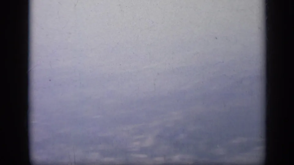 Soft, overexposed 1962 8mm travel frame in Italy showing pale sky and dark vehicle window edges before the church appears.