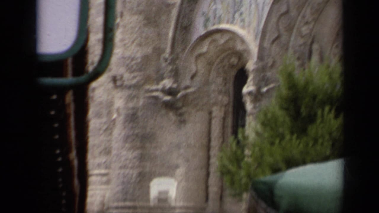 Stone church wall with arched opening, greenery, and dark foreground framing.