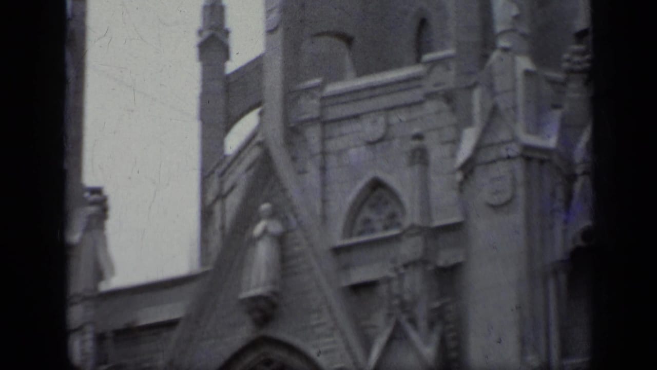 Upper stone church facade with pointed arch, spire, carved details, and dark film edge.