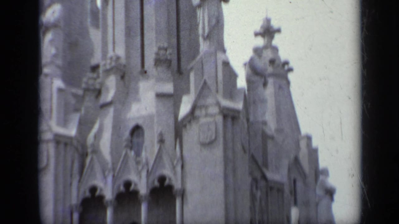 Church tower section with cross-topped stonework, arched openings, statues, and vertical facade details.