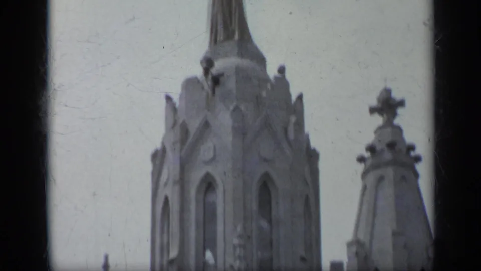 1962 Italy 8mm frame of the church's upper stonework, including pointed openings, sculptural figures, decorative pinnacles, and a cross-topped feature.