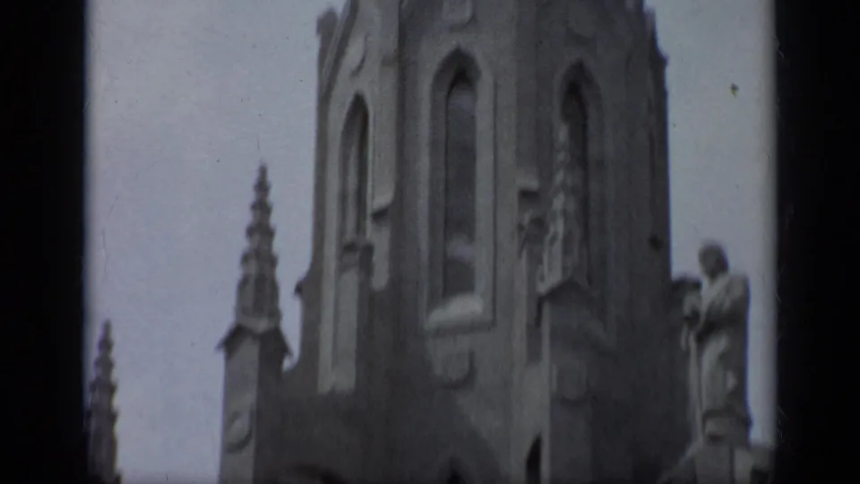 1962 Italy 8mm frame showing the cathedral's upper facade, arched openings, stone pinnacles, and sculptural figures from below.