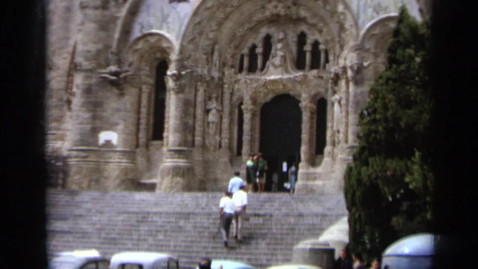1962 Italy 8mm frame showing visitors on steps approaching a large arched church doorway beneath carved stonework.