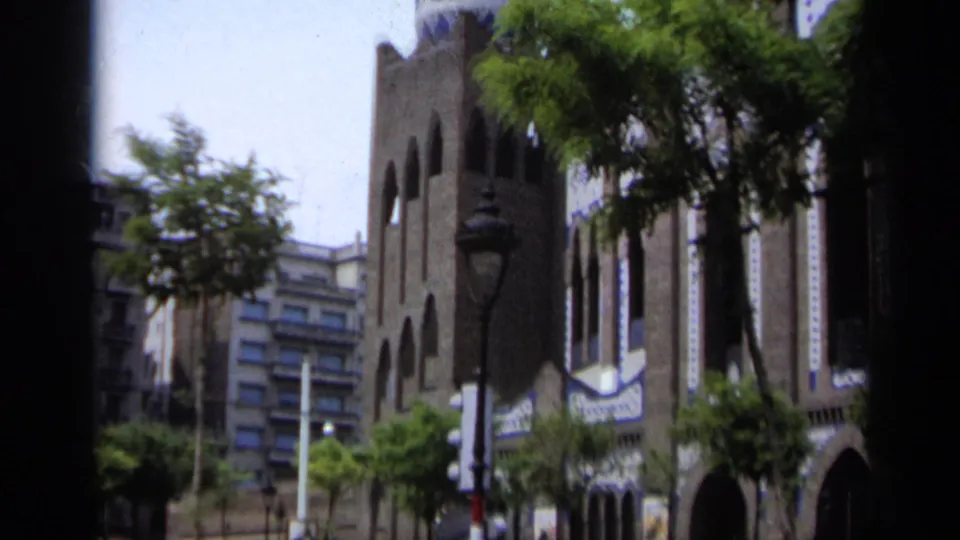 1962 Italy home-movie frame showing a colorful Gothic-style facade with arched windows, decorative trim, trees, and street lamps.