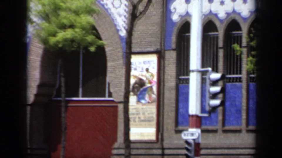 1962 Italy street view of a decorated brick facade with arched windows, blue panels, trees, traffic lights, and a bullfight poster.