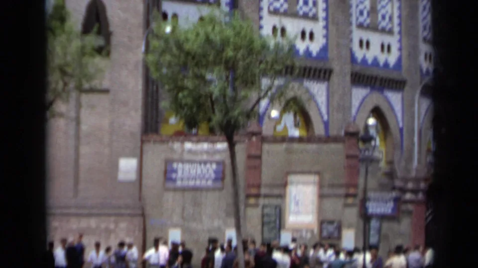 1962 Italy street crowd outside an ornate blue-and-white brick facade with arched openings, posters, trees, and street fixtures.