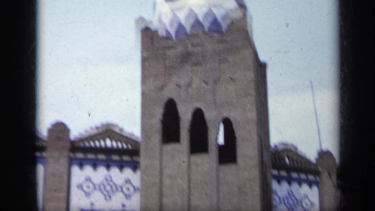 Upper section of a tower-like monument with arched openings and patterned roof trim.