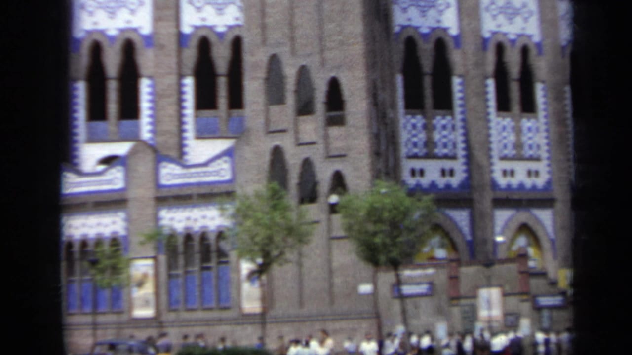 Closer view of the arena facade with trees and people near the entrance.