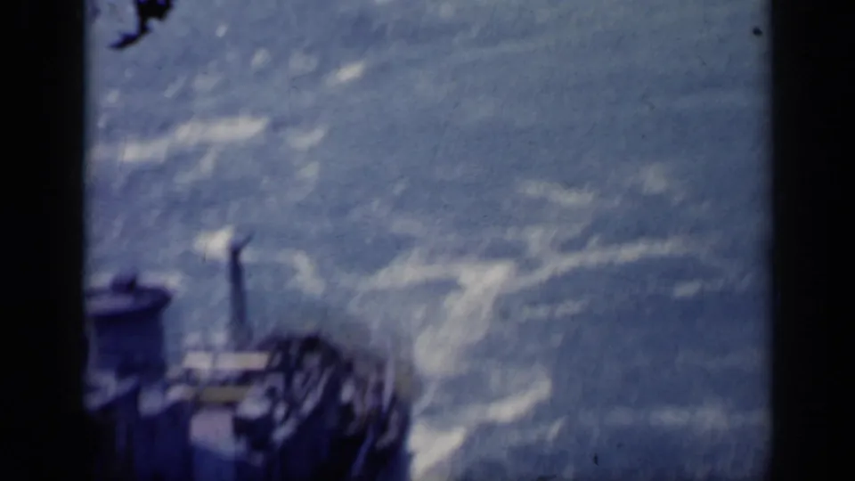 1962 Italy 8mm frame with a dark vessel edge or deck detail beside bright, foaming water in soft focus.