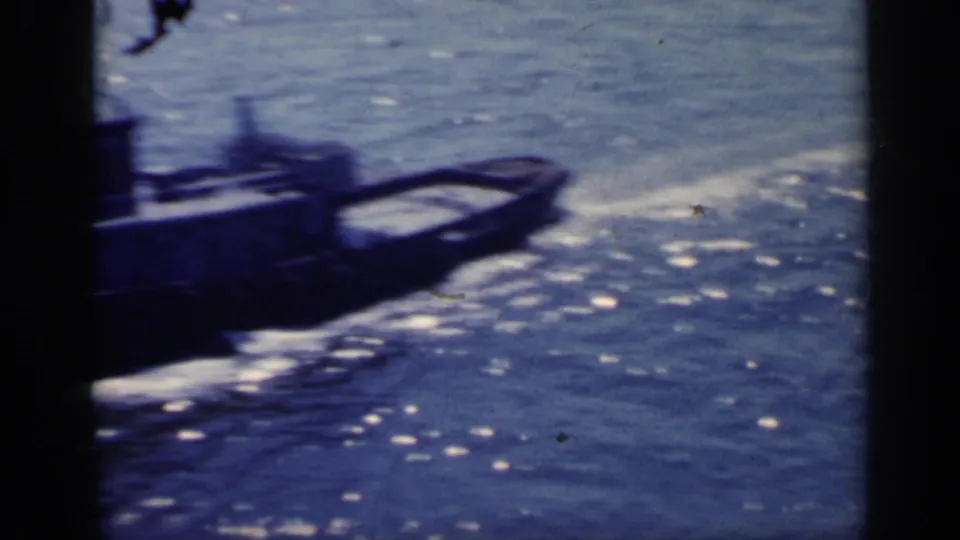 1962 Italy 8mm frame with a small industrial boat moving close to camera across rippled blue water, partly obscured by frame edge.