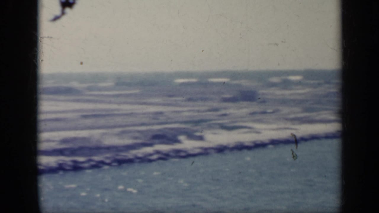 Choppy water and a low shoreline seen through a dark film-frame edge.