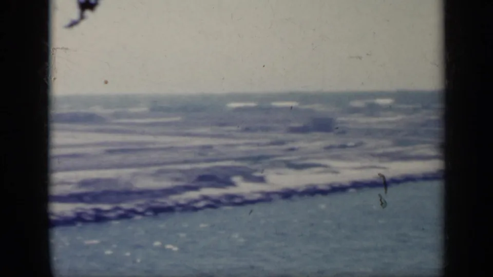 1962 Italy 8mm frame with choppy coastal water, a low rocky shore, and dark vertical frame edging from the film scan.