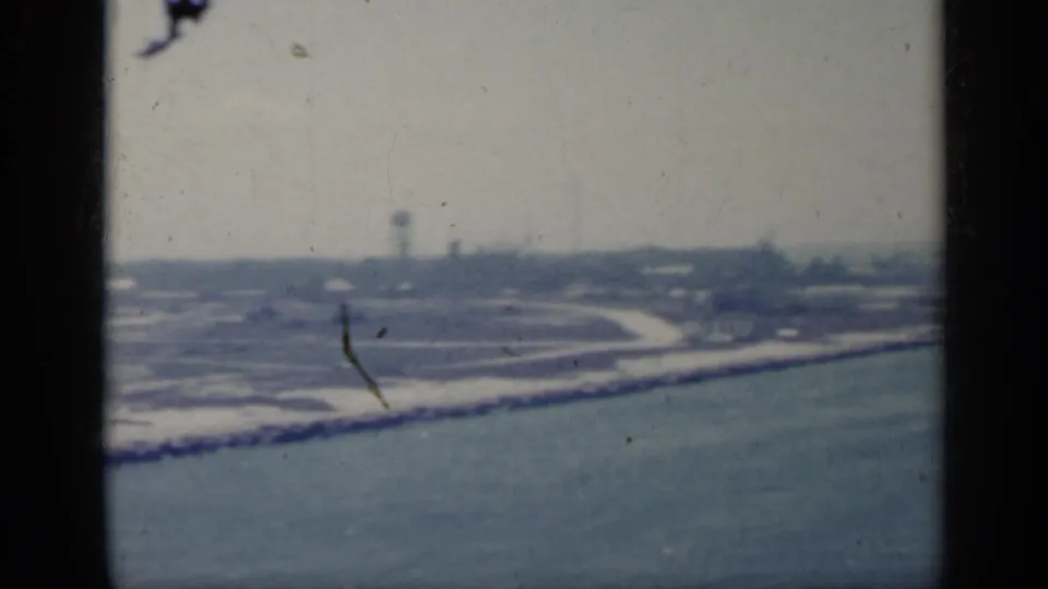 1962 Italy 8mm frame showing a hazy coastal horizon, breakwater, water, and faint distant structures.