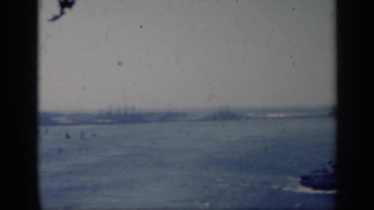 Distant harbor view with a small tugboat on the water and an aircraft carrier at right.