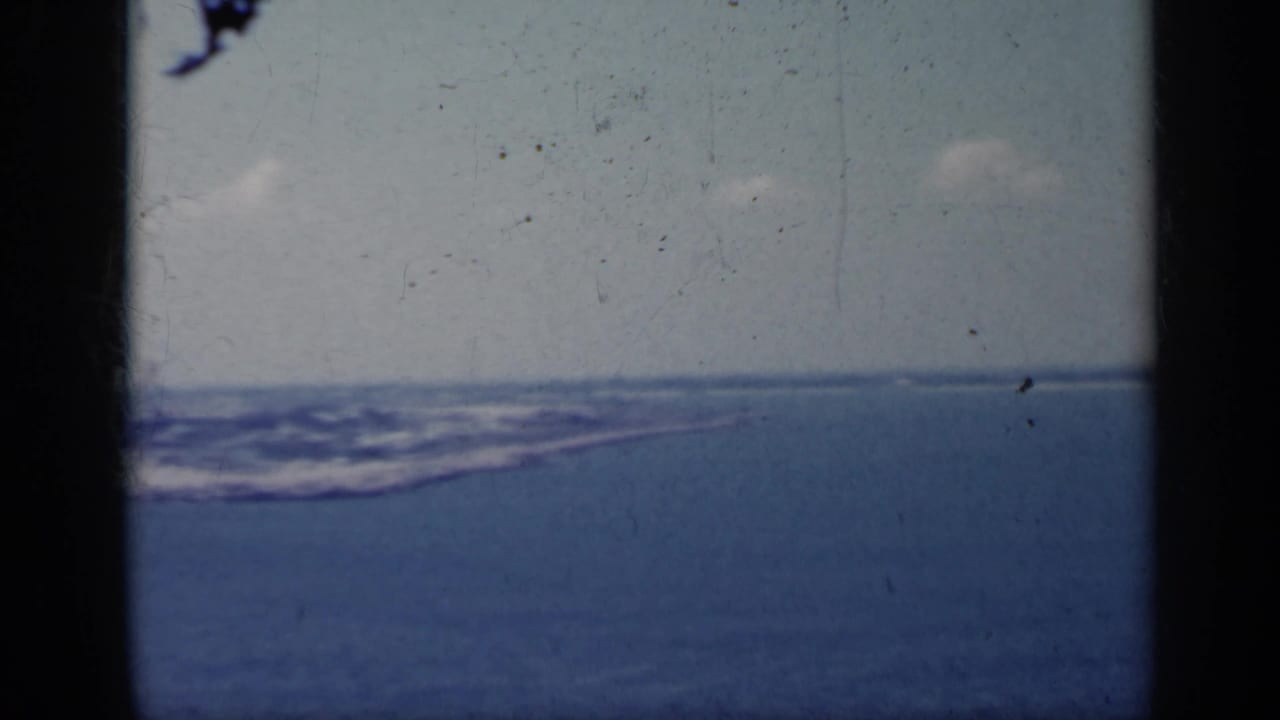 Blue sea and distant coastline seen through dark film-frame edges.
