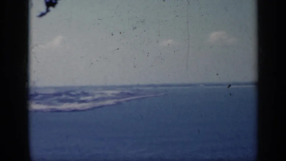 1962 Italy 8mm frame showing open blue water, a pale sky, and a low distant coastline through visible gate edges.