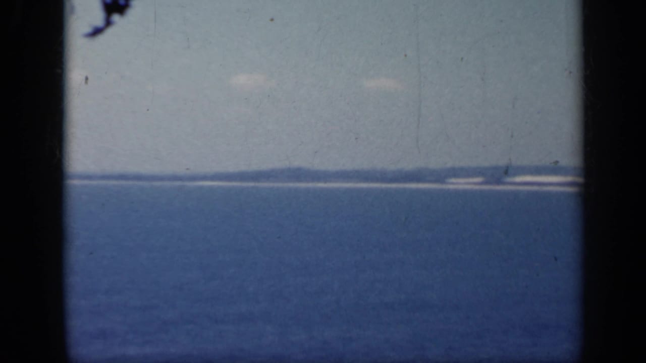 1962 Italy coastal view with blue water, faint land on the horizon, and visible film wear from the scanned 8mm source.