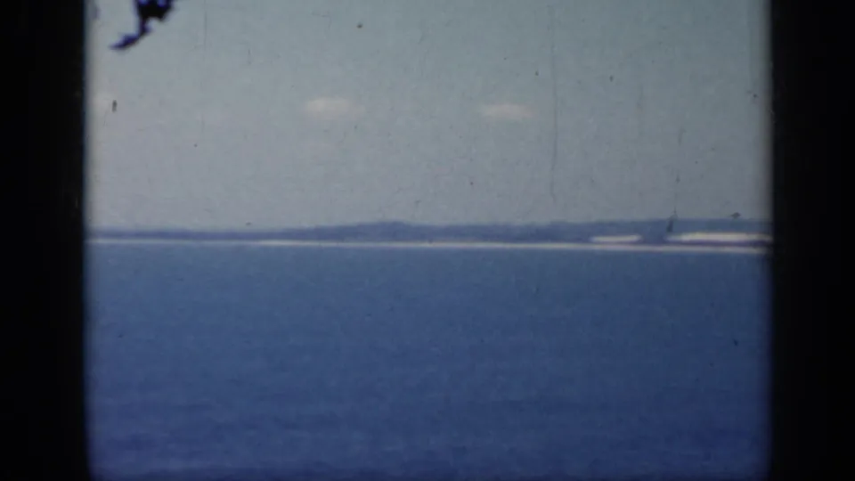 1962 Italy coastal view with blue water, faint land on the horizon, and visible film wear from the scanned 8mm source.