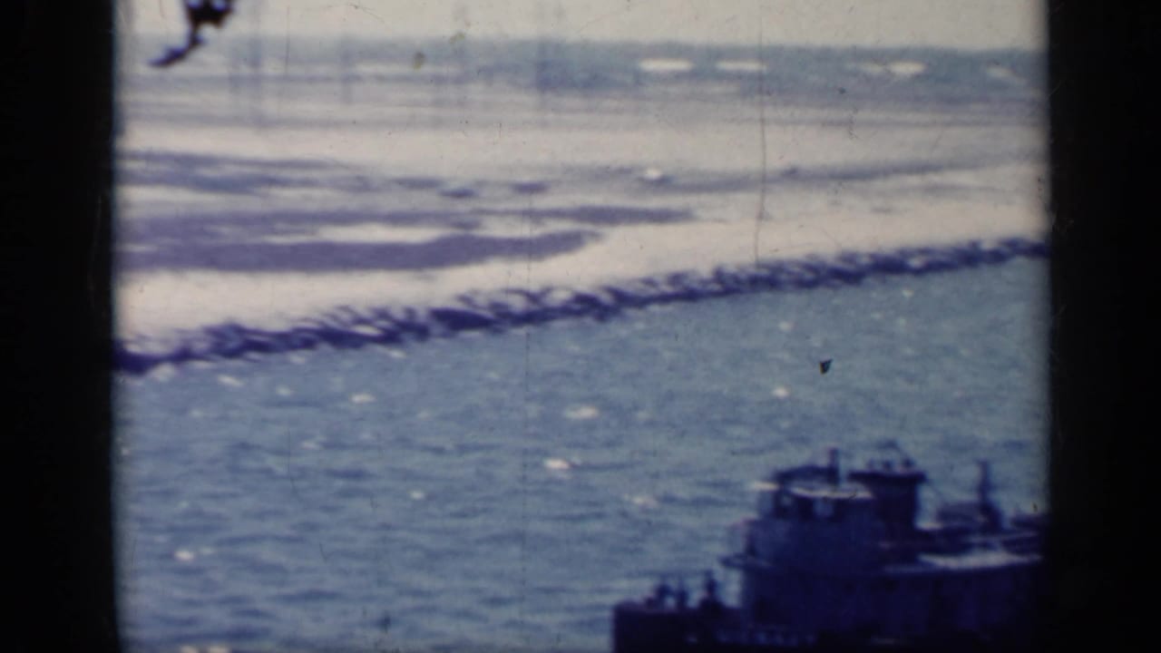 Coastal water with a dark tugboat near a rocky shoreline, seen through dark vertical frame bars.