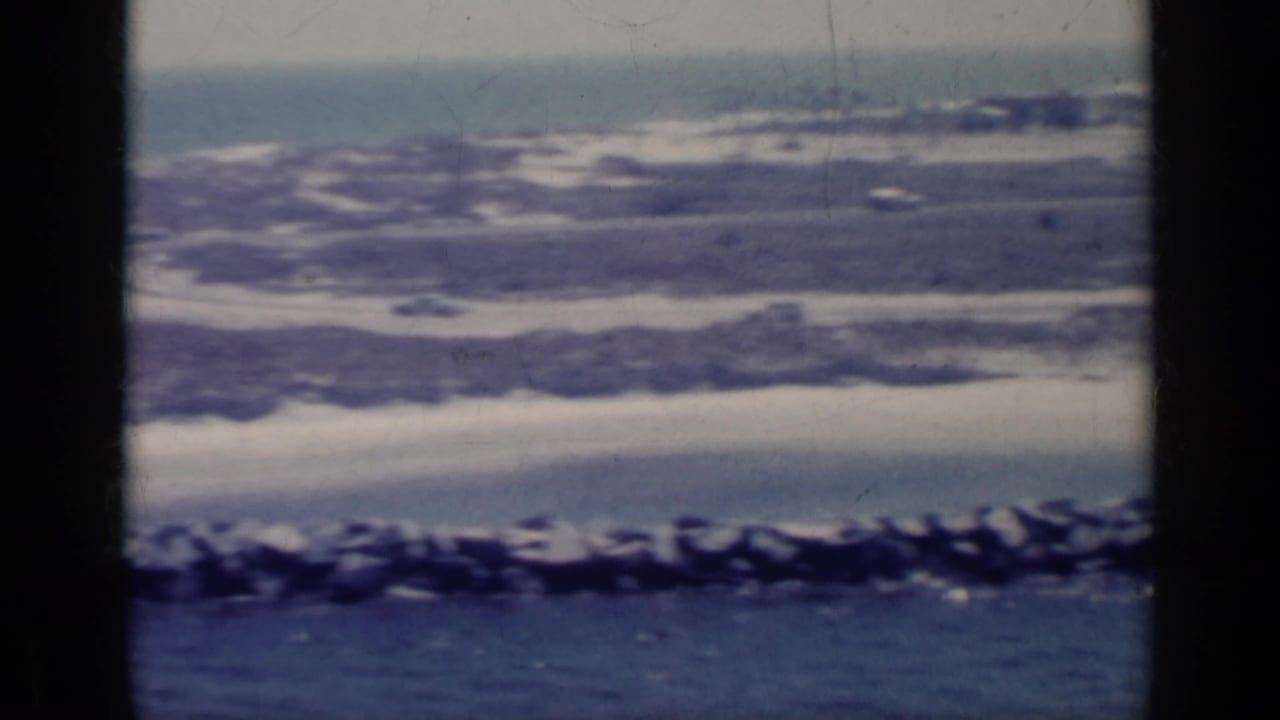 Distant coastal strip with waves, rocks, blue water, and dark film-frame borders.