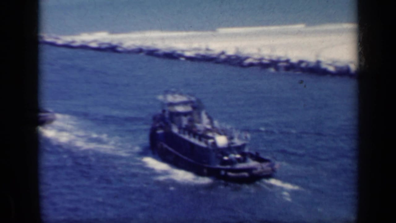 Small tugboat moving through blue water near a rocky breakwater.