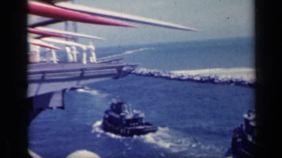 1962 Italy 8mm frame showing red and white ship masts over blue water with tugboats moving below.