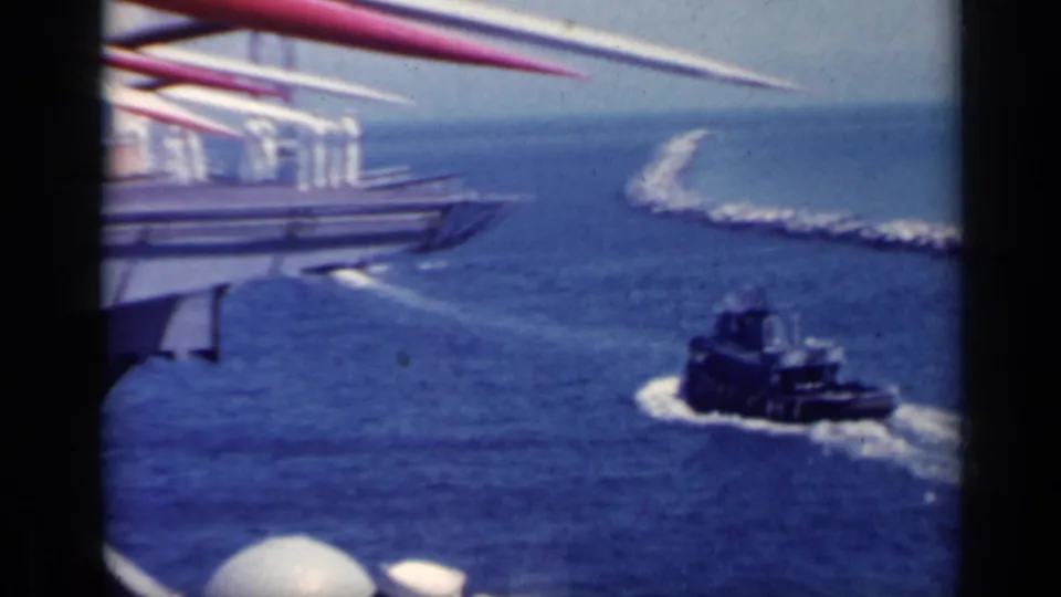 1962 Italy 8mm frame with a tugboat turning below red and white ship masts near a curved breakwater.