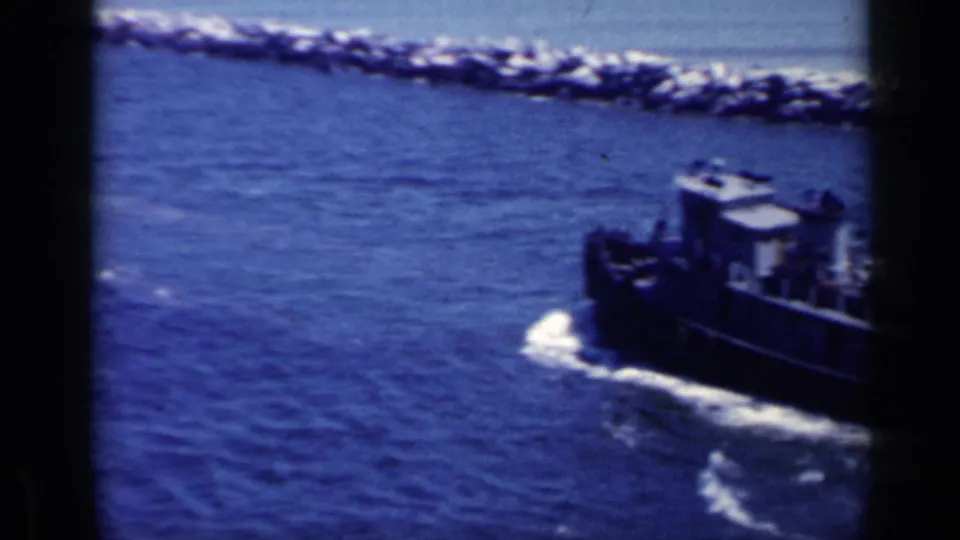 Closer 8mm view of a working tugboat in blue harbor water, partially framed by dark vertical film or scan borders.