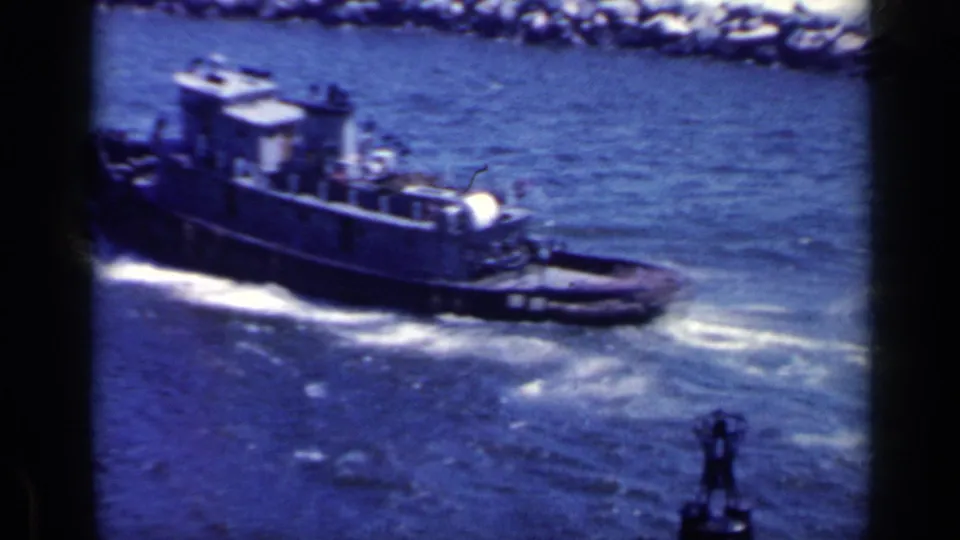 A tugboat passes close below in the Italian harbor scene, leaving wake beside the jetty, with a small deck fitting in the foreground.