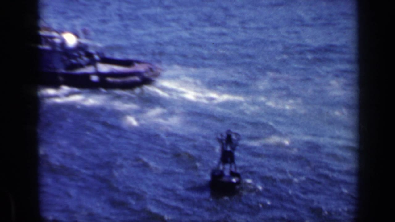 Small boat on choppy blue water near a dark buoy and visible film edge.