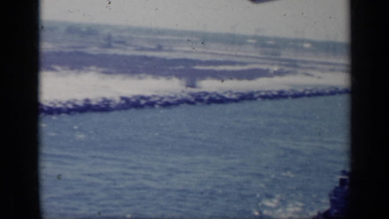 Distant coastline and surf seen across blue water with dark film borders.