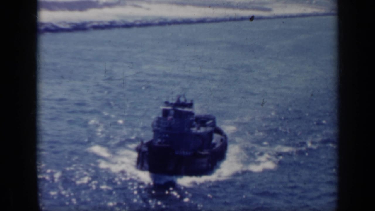 Small dark boat moving across calm water near a surf line.