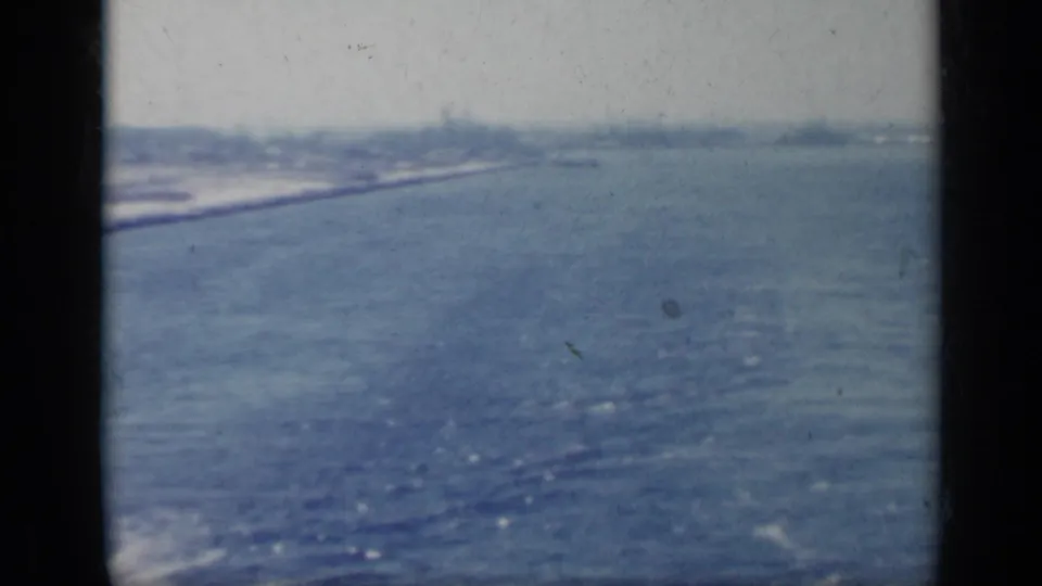 1962 Italy 8mm frame showing a wide, distant coastal view across calm water with soft blue fading.