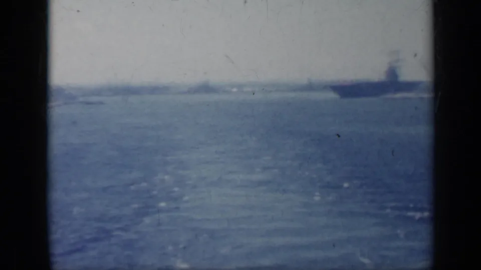 1962 Italy 8mm frame showing a large distant naval ship offshore on calm water under a hazy sky.