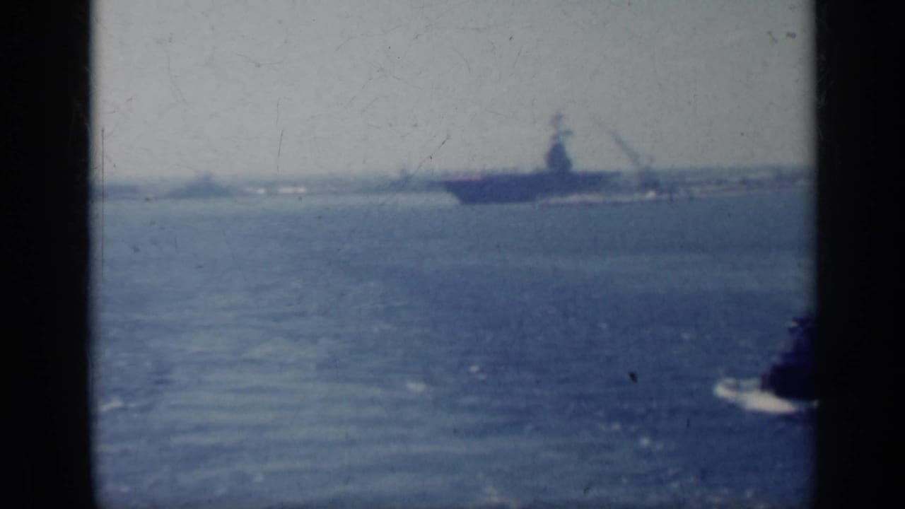 Distant aircraft carrier on the horizon with a small vessel crossing open water.