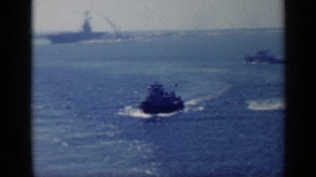 Small boat moves across open water with a larger ship faint on the horizon.