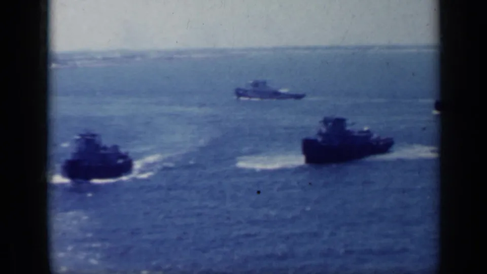 1962 Italy 8mm frame showing multiple tugboat-like support vessels moving across open water with wakes behind them.
