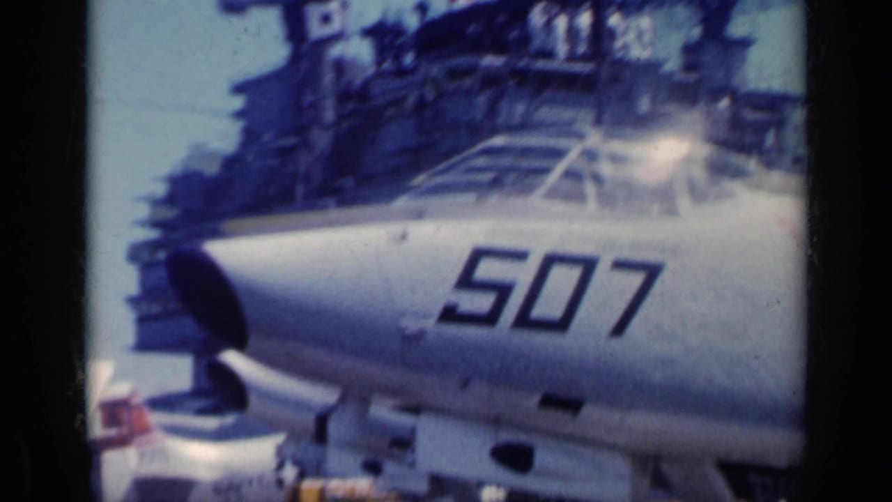 Close 1962 Italy frame of a carrier-based military jet nose marked 507, with the ship island structure behind it.