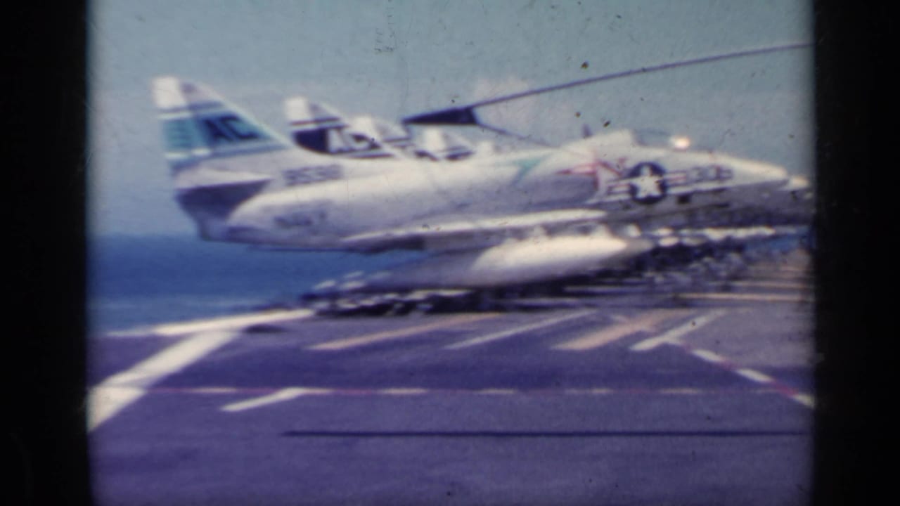 Military jet on an aircraft carrier deck with ocean visible beyond.