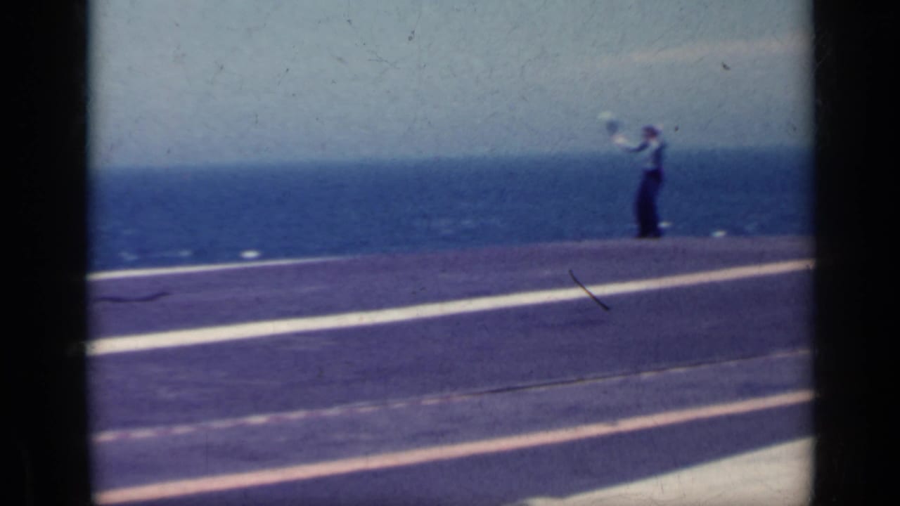 Carrier flight deck with a crew member standing near the ocean horizon.
