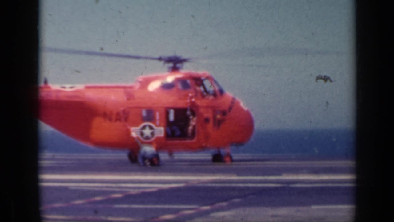 Red Navy helicopter on an aircraft carrier deck with a person near the nose.