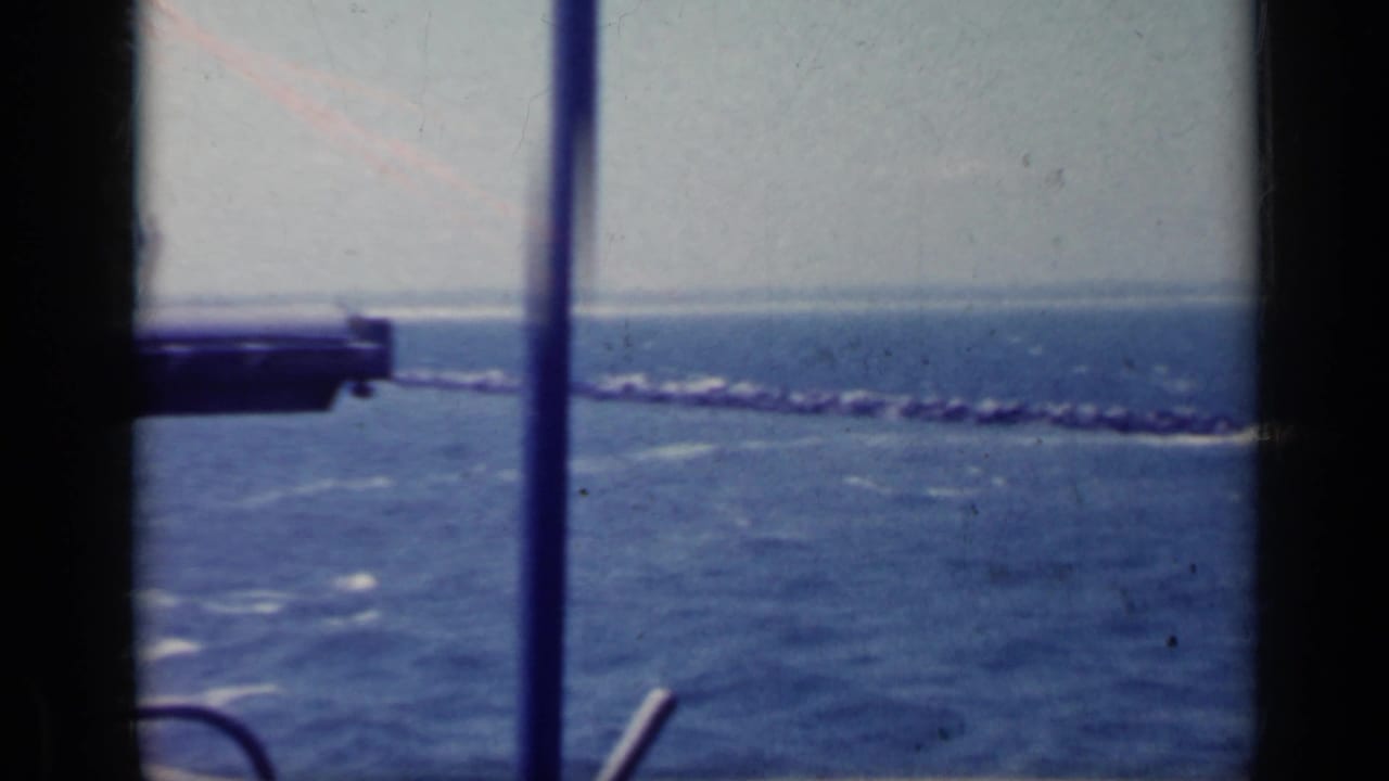 View over blue water and distant shore through a dark boat window frame.