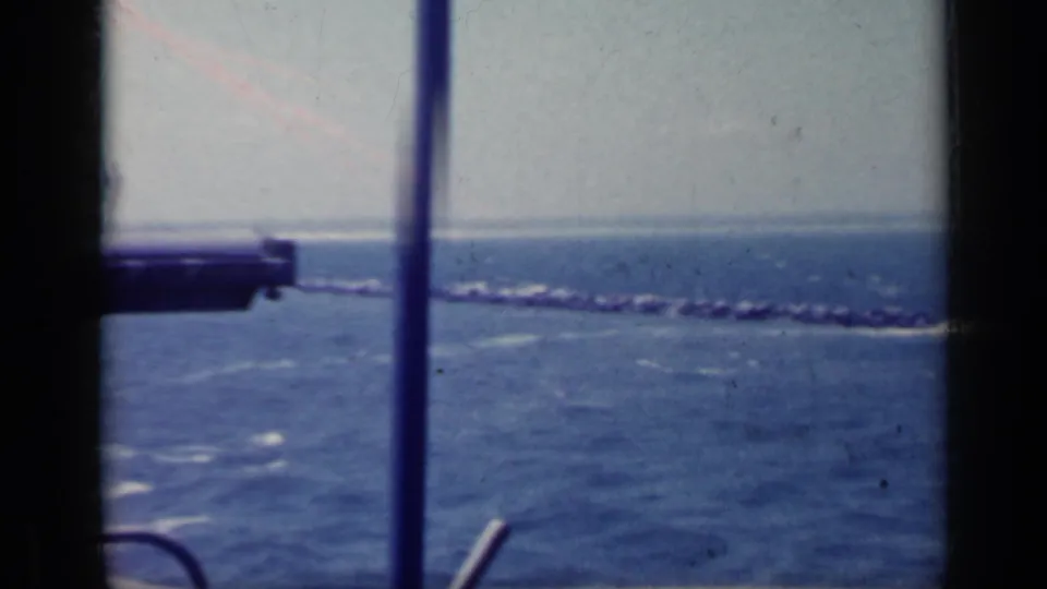 1962 Italy home-movie frame looking from a boat window toward open water, horizon, and a distant coastline.