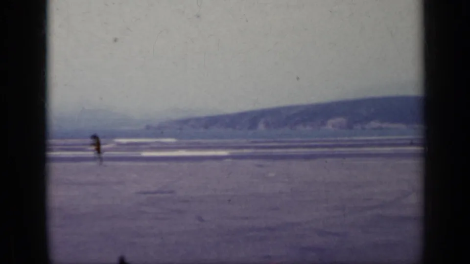 1962 Italy home-movie frame with a lone distant figure on a broad runway-like surface, with hills and pale sky in the background.